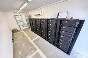 Innenansicht eines Technikraums mit mehreren Batterieschränken des FENECON Commercial Speichersystems, Elektroverteilung und Wandklimagerät