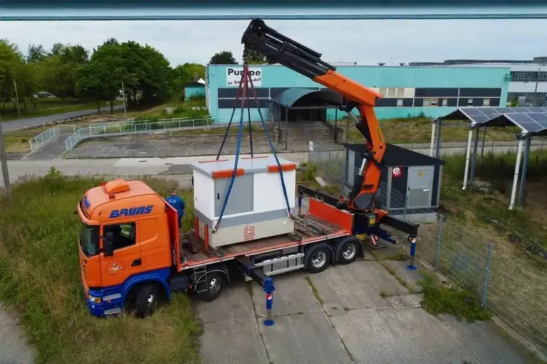 GRYTEC Container wird mit einem Kran auf einem LKW entladen – Beispiel für die Anlieferung stationärer Energie- oder Trafostationen.