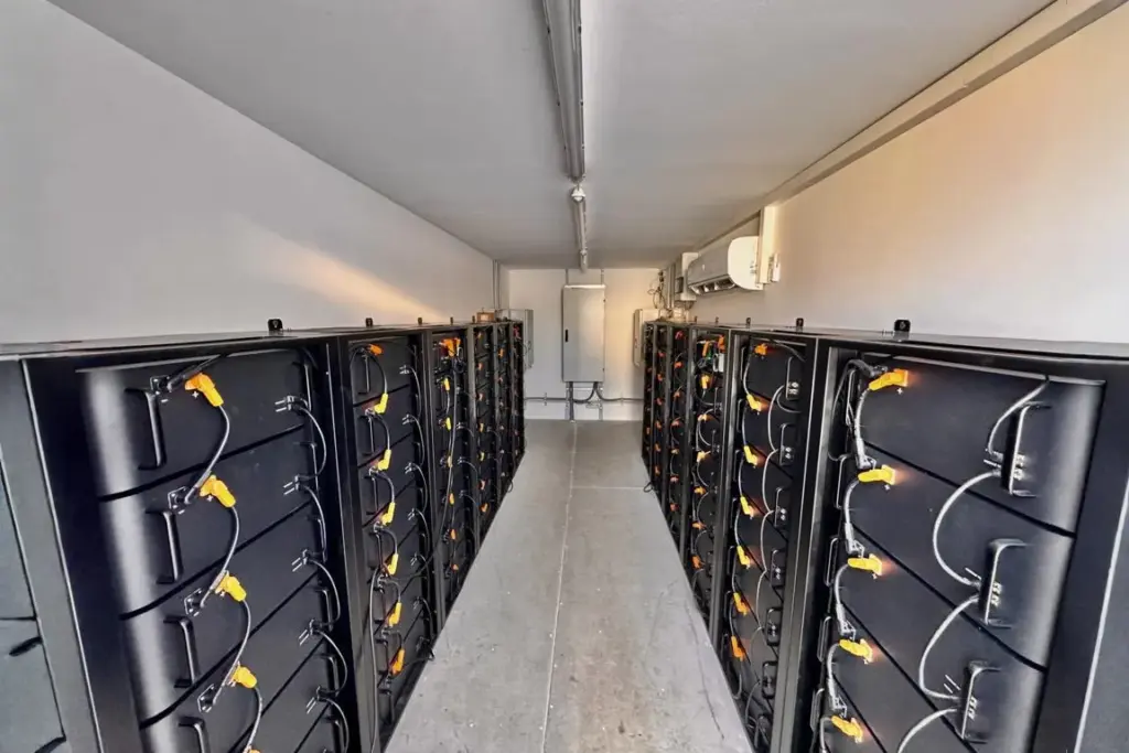 Blick in einen langen Technikraum mit zwei Reihen FENECON Commercial Batterieschränken, zentralem Gang und Klimagerät an der Wand