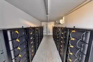 Blick in einen langen Technikraum mit zwei Reihen FENECON Commercial Batterieschränken, zentralem Gang und Klimagerät an der Wand