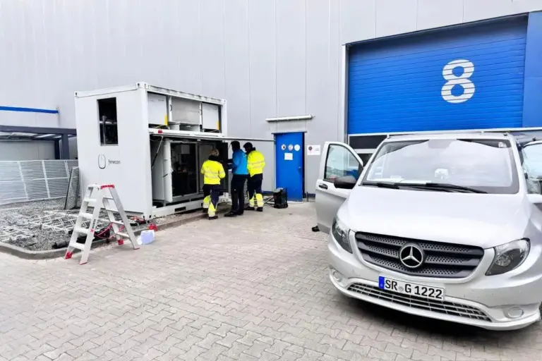 Techniker beim Serviceeinsatz an einem geöffneten FENECON Industrial M Energiespeicher vor einem Industriegebäude mit Tor Nummer 8