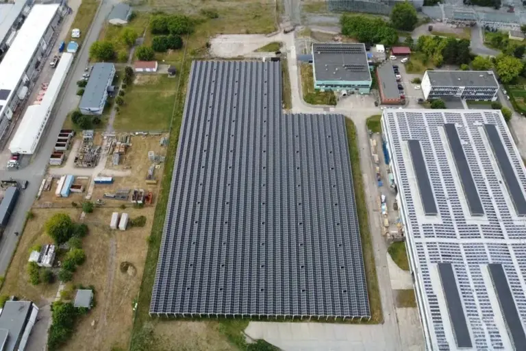 Freiflächen-Photovoltaikanlage neben Industriehallen, Luftaufnahme
