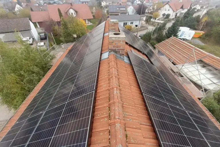 Photovoltaikanlage auf rotem Ziegeldach mit Kamin in einem Wohngebiet, Herbstlandschaft im Hintergrund