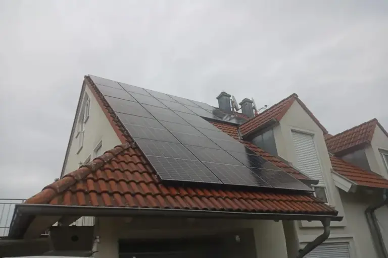 Photovoltaikanlage auf einem Wohnhaus mit rotem Ziegeldach und mehreren Dachgauben, montiert auf zwei geneigten Dachflächen bei bewölktem Himmel