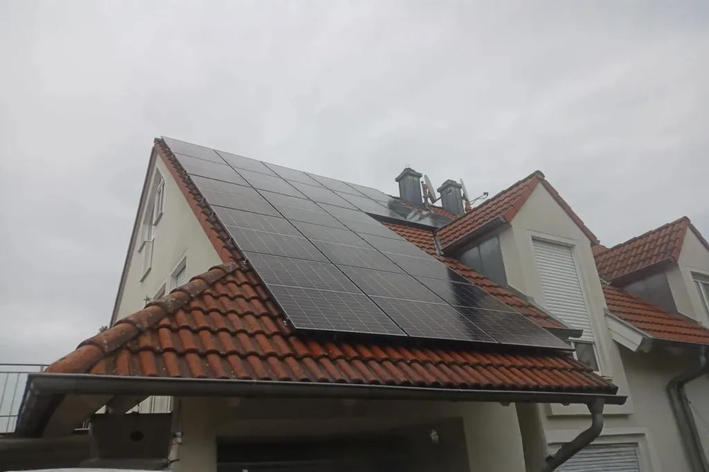 Photovoltaikanlage auf einem Wohnhaus mit rotem Ziegeldach und mehreren Dachgauben, montiert auf zwei geneigten Dachflächen bei bewölktem Himmel