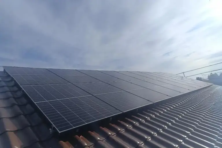 Photovoltaikanlage auf braunem Ziegeldach bei klarem Himmel, geneigte Dachfläche mit vollständig belegten PV-Modulen