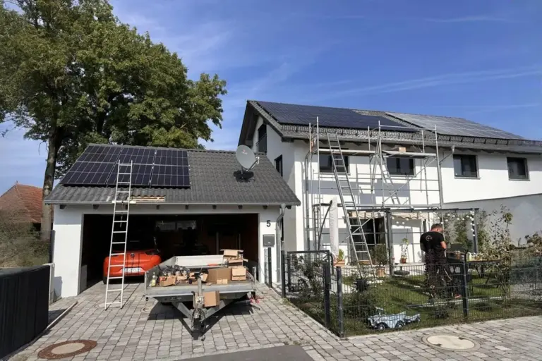 Montage einer Photovoltaikanlage auf Wohnhaus und Garage mit grauem Ziegeldach; Gerüst, Leiter und Monteur vor Ort sichtbar